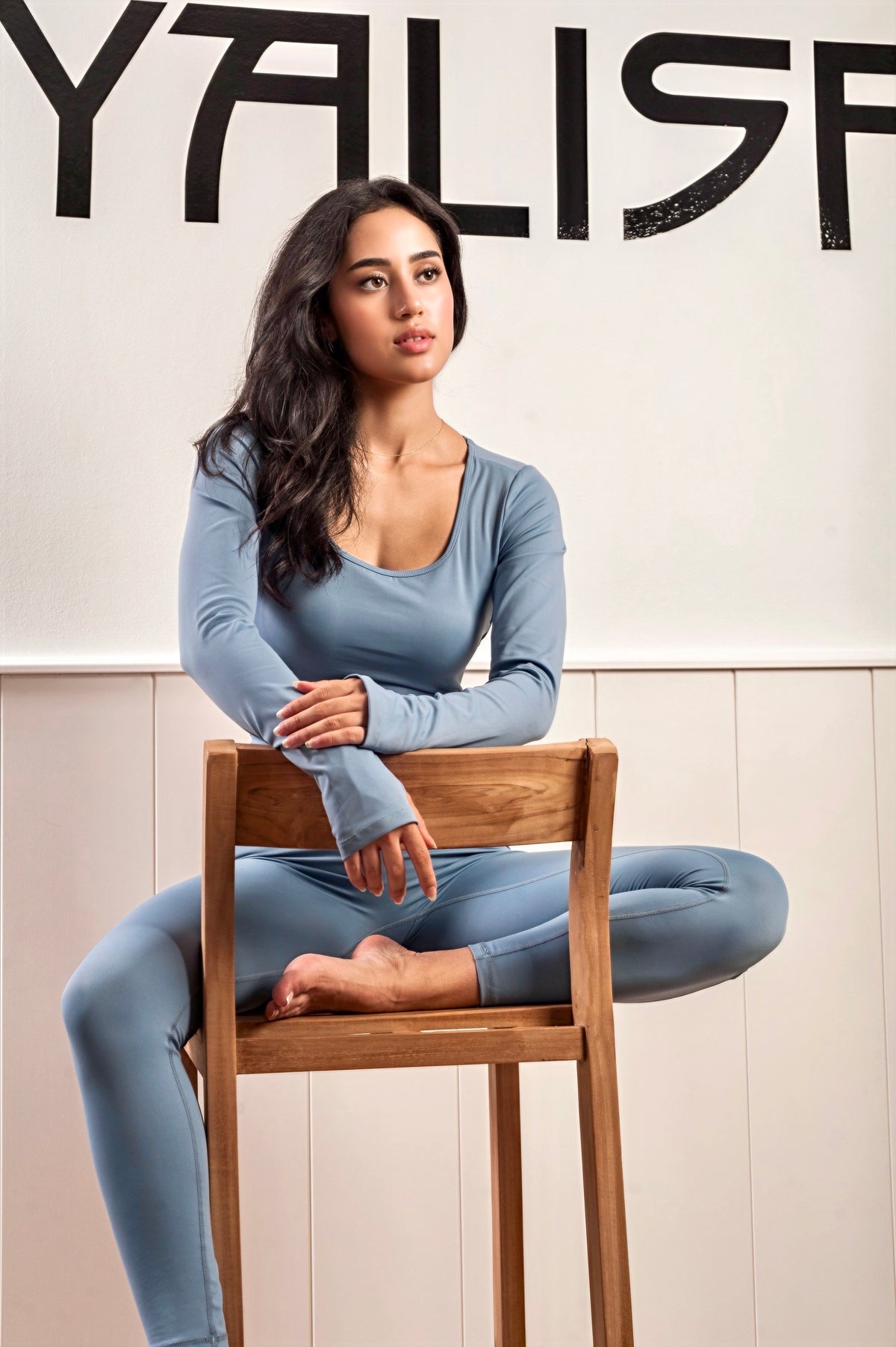 Mujer sentada en un taburete viste un mono de yoga de color azul 
